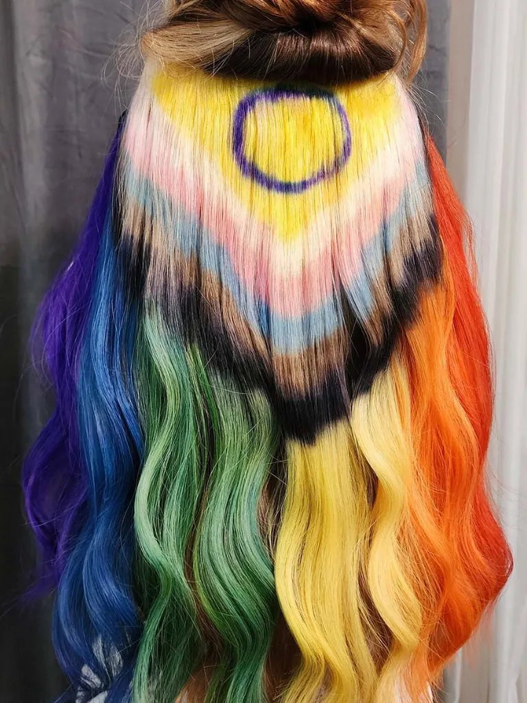 Back of model’s head, the Progress Pride flag has been painted through their long, straight hair.