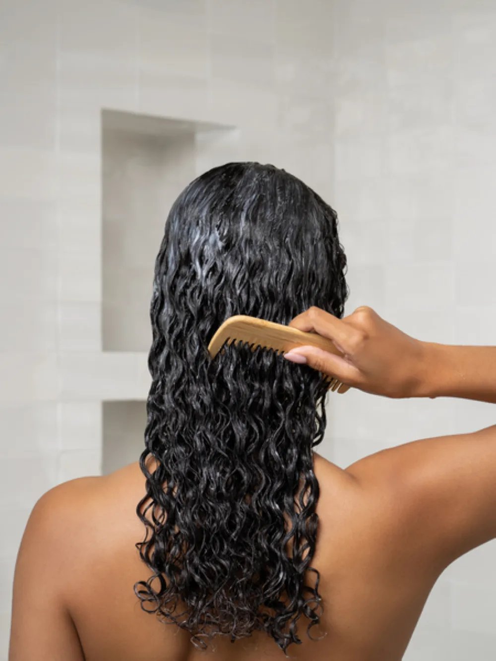 Model detangling wet curly hair with a comb during a hair care routine