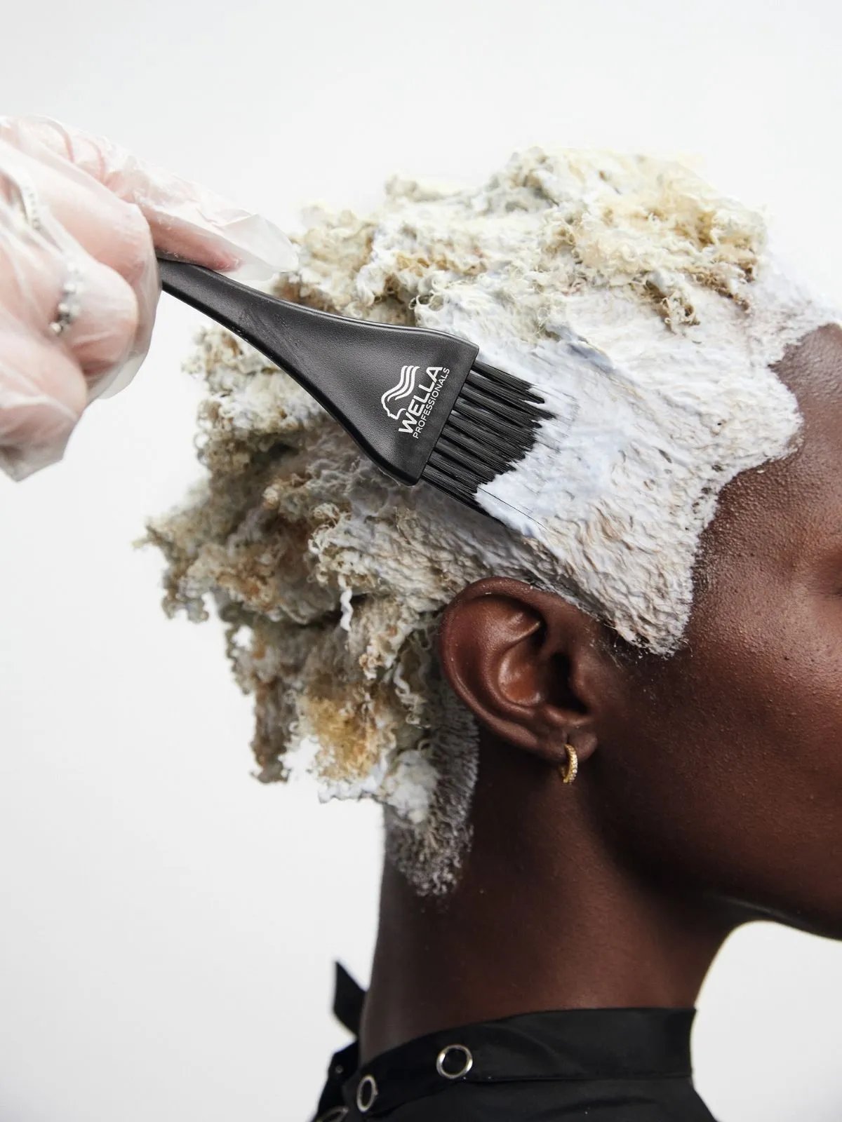 BlondorPlex lightener is applied to a model’s dark, coily hair using a Wella tint brush.