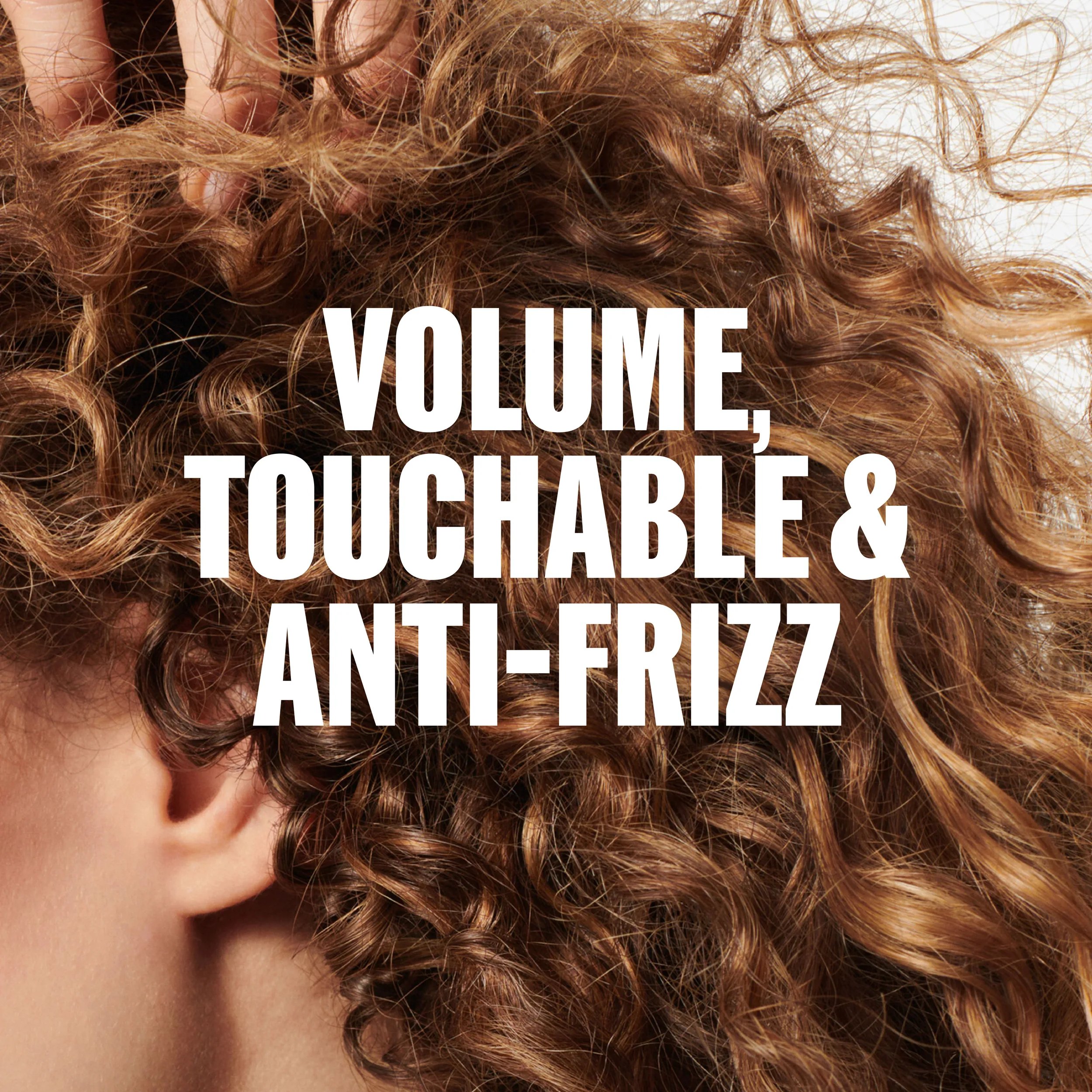 Close-up of curly, textured brown hair with the text “VOLUME TOUCHABLE & ANTI-FRIZZ" overlaid in white.