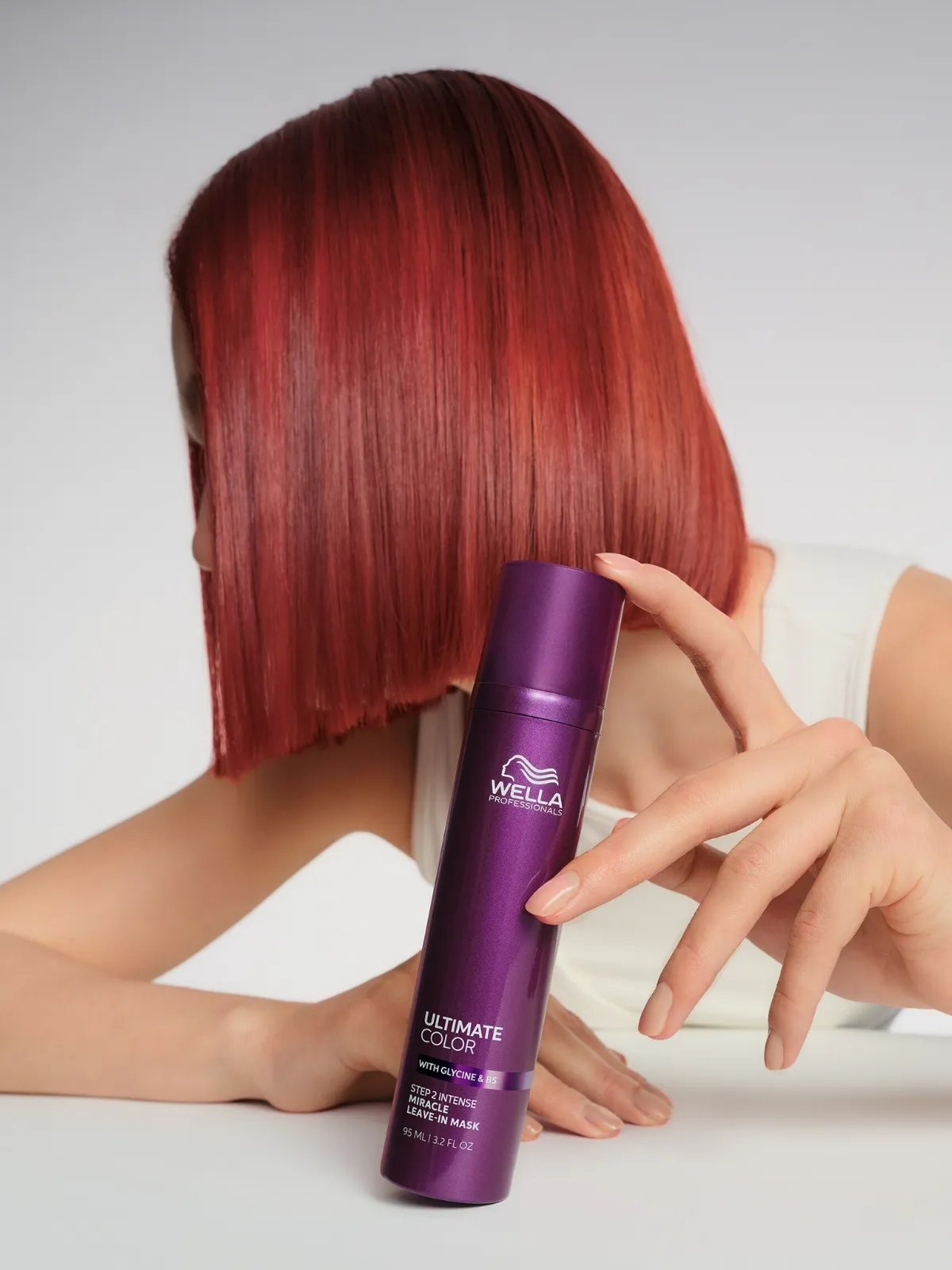 Model with bright red hair holds a bottle of ULTIMATE COLOR Miracle Leave-In Mask.
