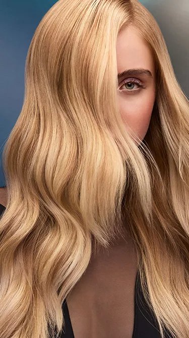 Mujer con cabello rubio largo y ondulado, sobre un fondo azul difuso.