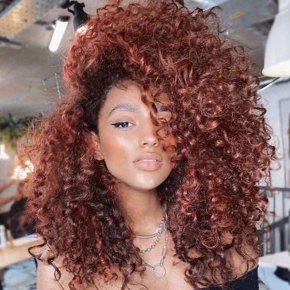 Woman facing the camera with curly, copper red hair, created using Wella Professionals.
