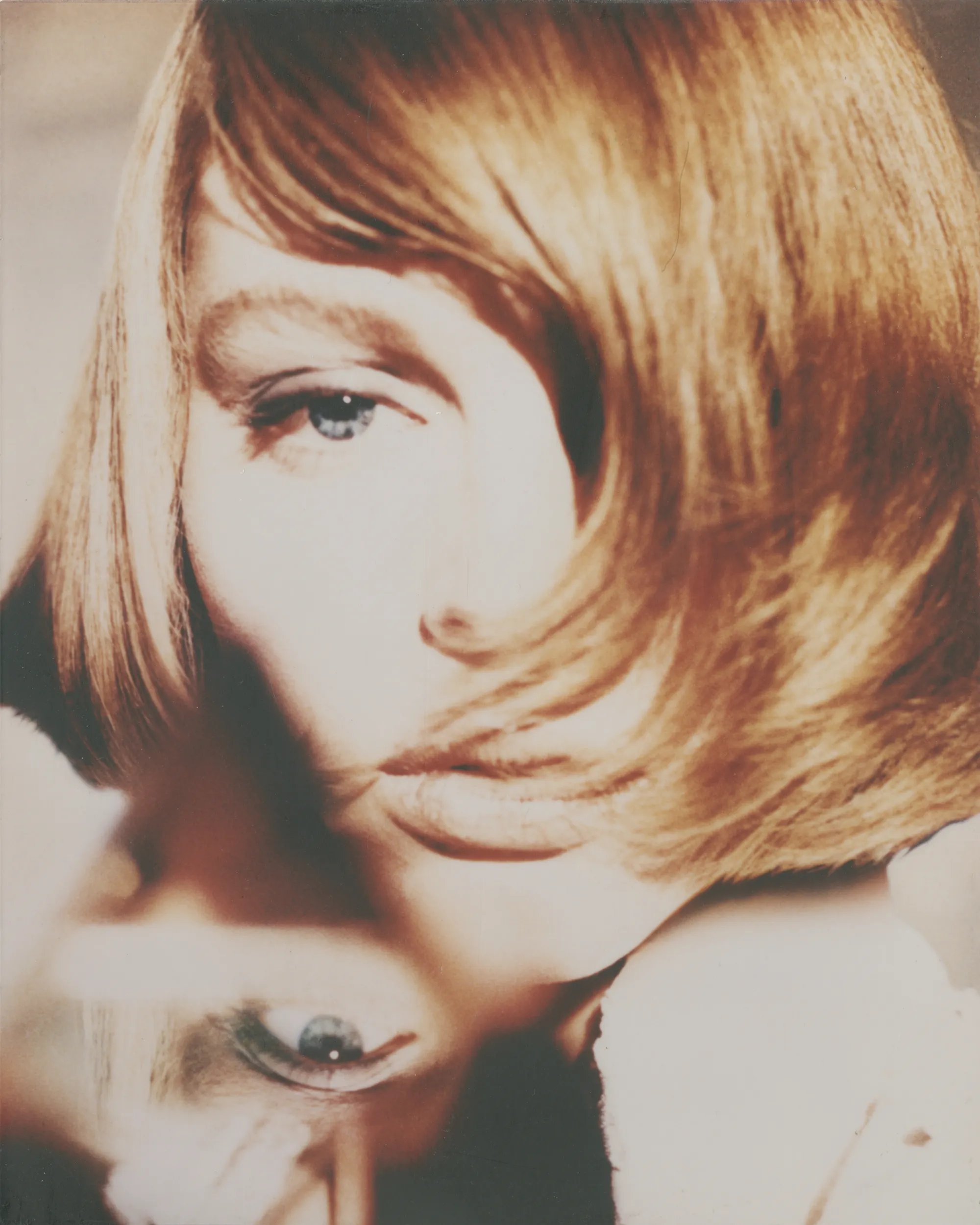 Model with short hair covering half of her face, only revelaing one eye. Reflection of the model's eye is in the bottom right corner. 