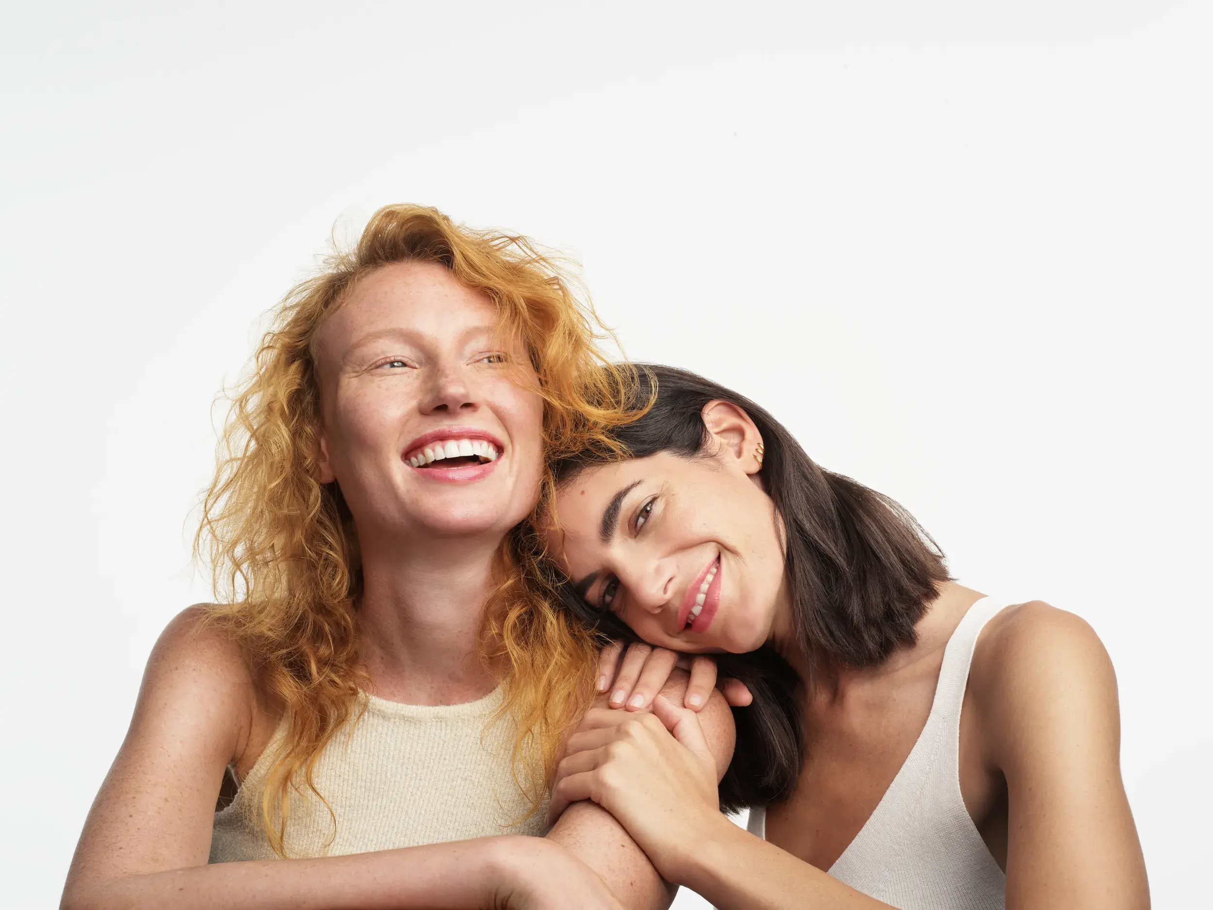 white brunette woman lying on the shoulder of a white ginger woman both smiling