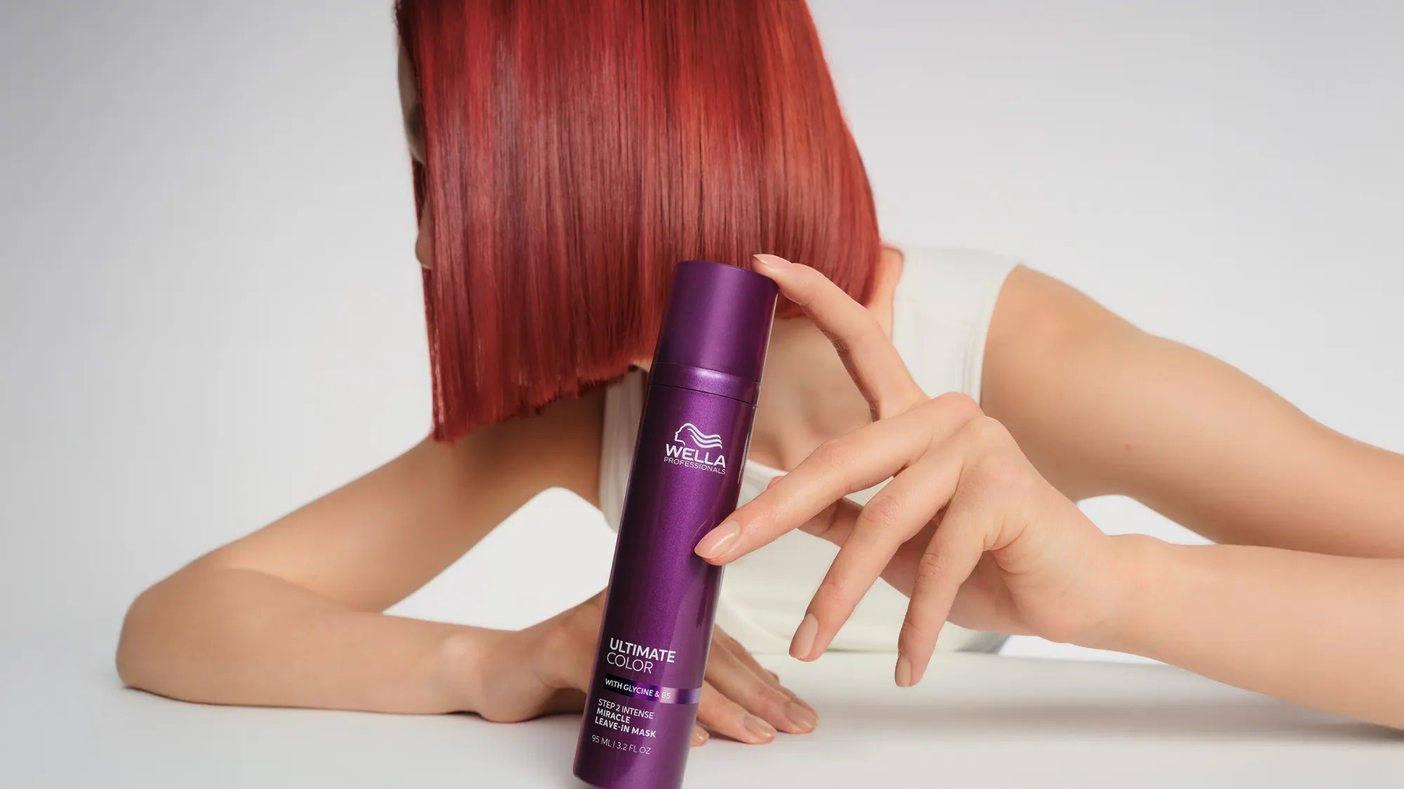 Model with bright red bob haircut holds a bottle of ULTIMATE COLOR Miracle Leave-In Mask. 