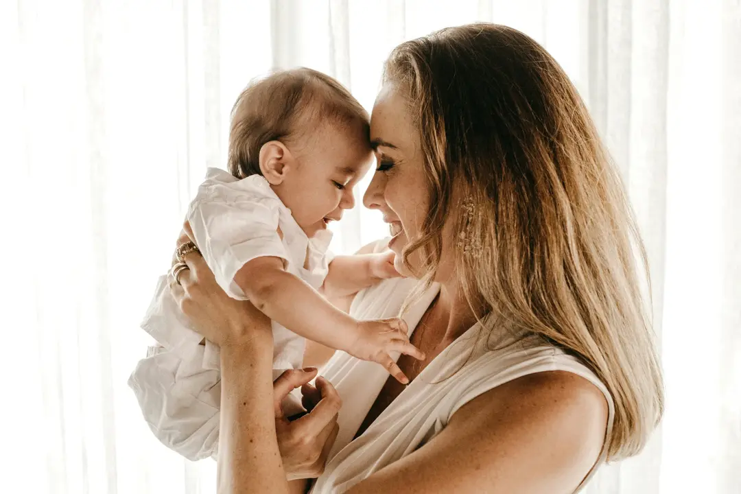 white woman smiling holding baby with foreheads together