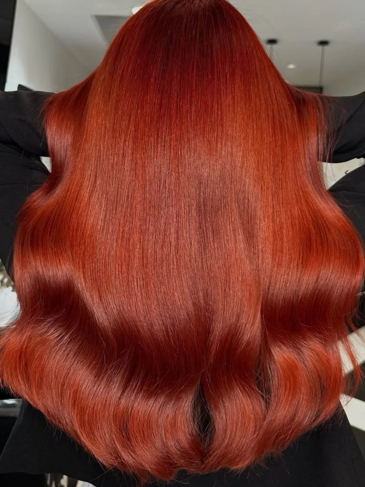 Back of model’s head showing long, glossy, blood orange-colored hair.