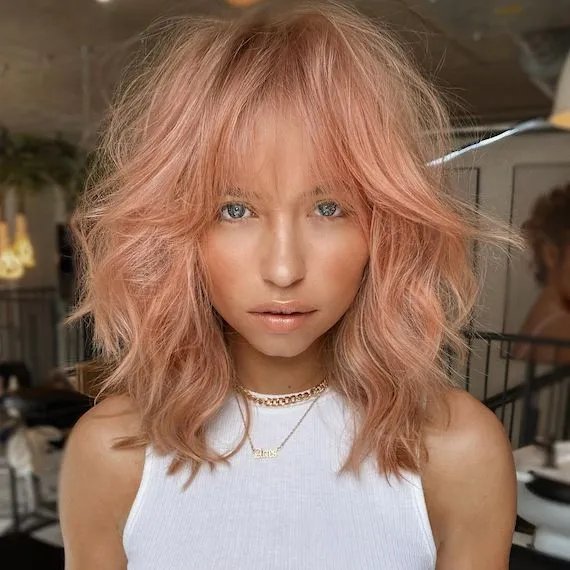 Model with tousled, wavy, pastel hair featuring rose gold, peach and strawberry blonde hues.