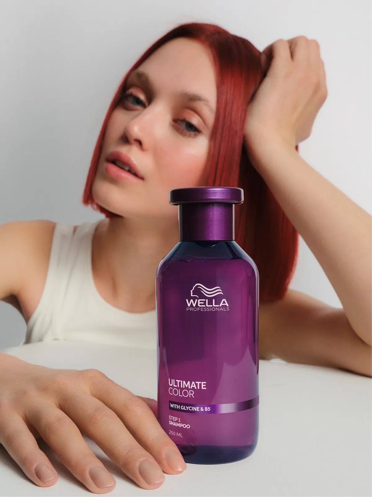 Model with bright red hair holds a bottle of ULTIMATE COLOR Shampoo.