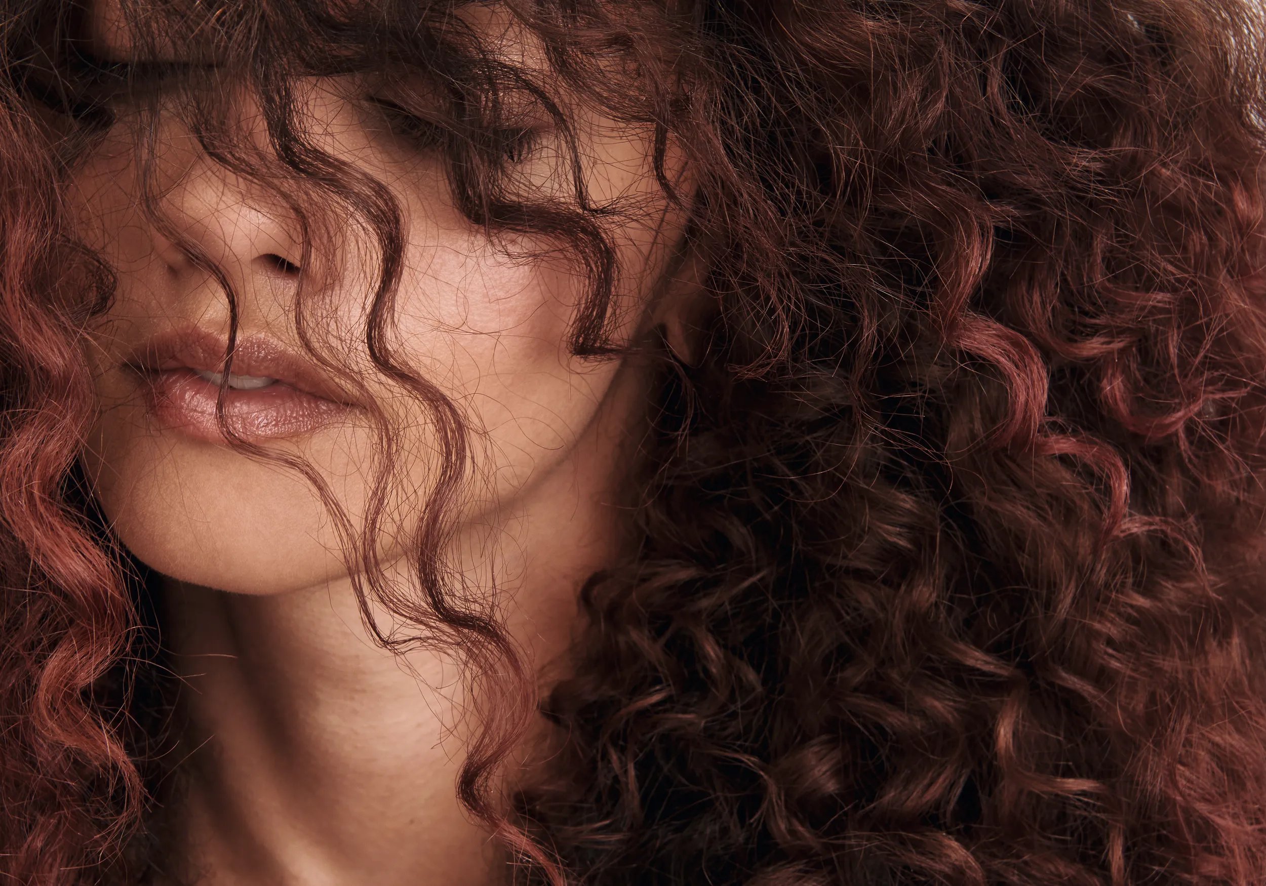Close-up of wavy auburn-colored hair against a light background.