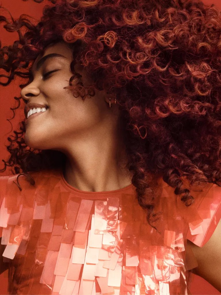 Model smiles while swishing their red-brown, curly hair. 