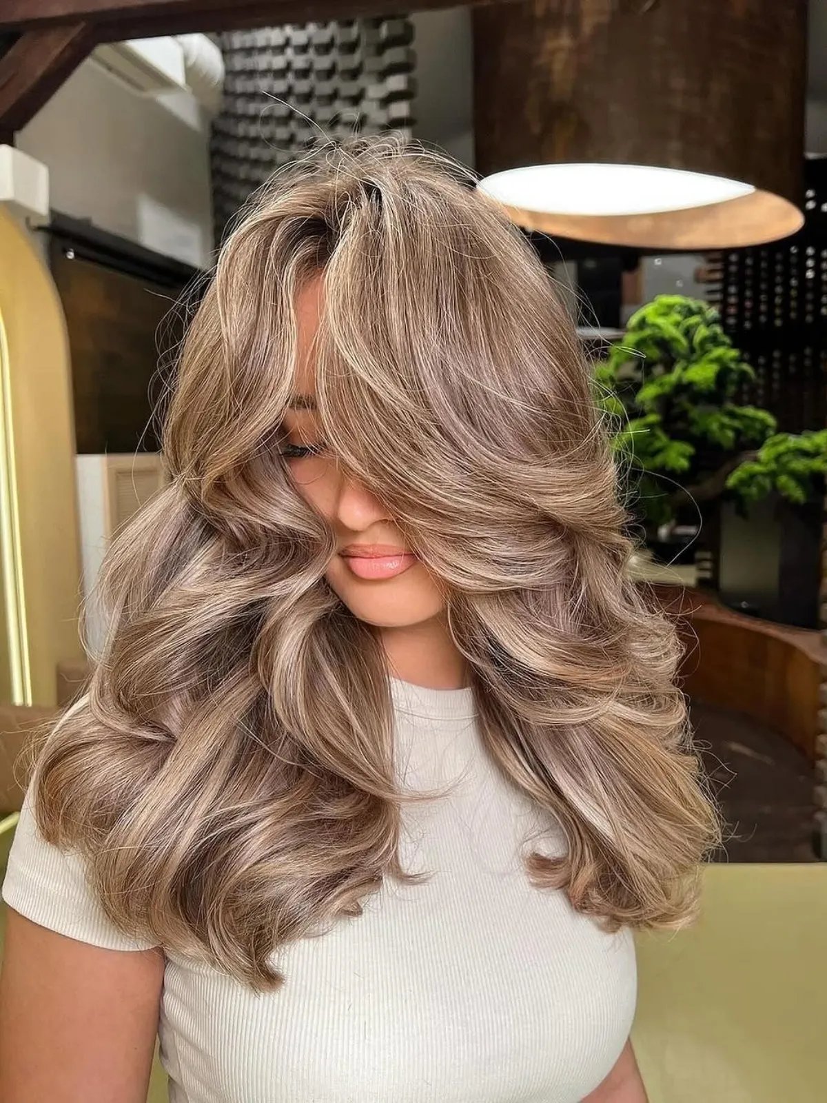 Model with voluminous, ash golden blonde curls shown from a different angle.