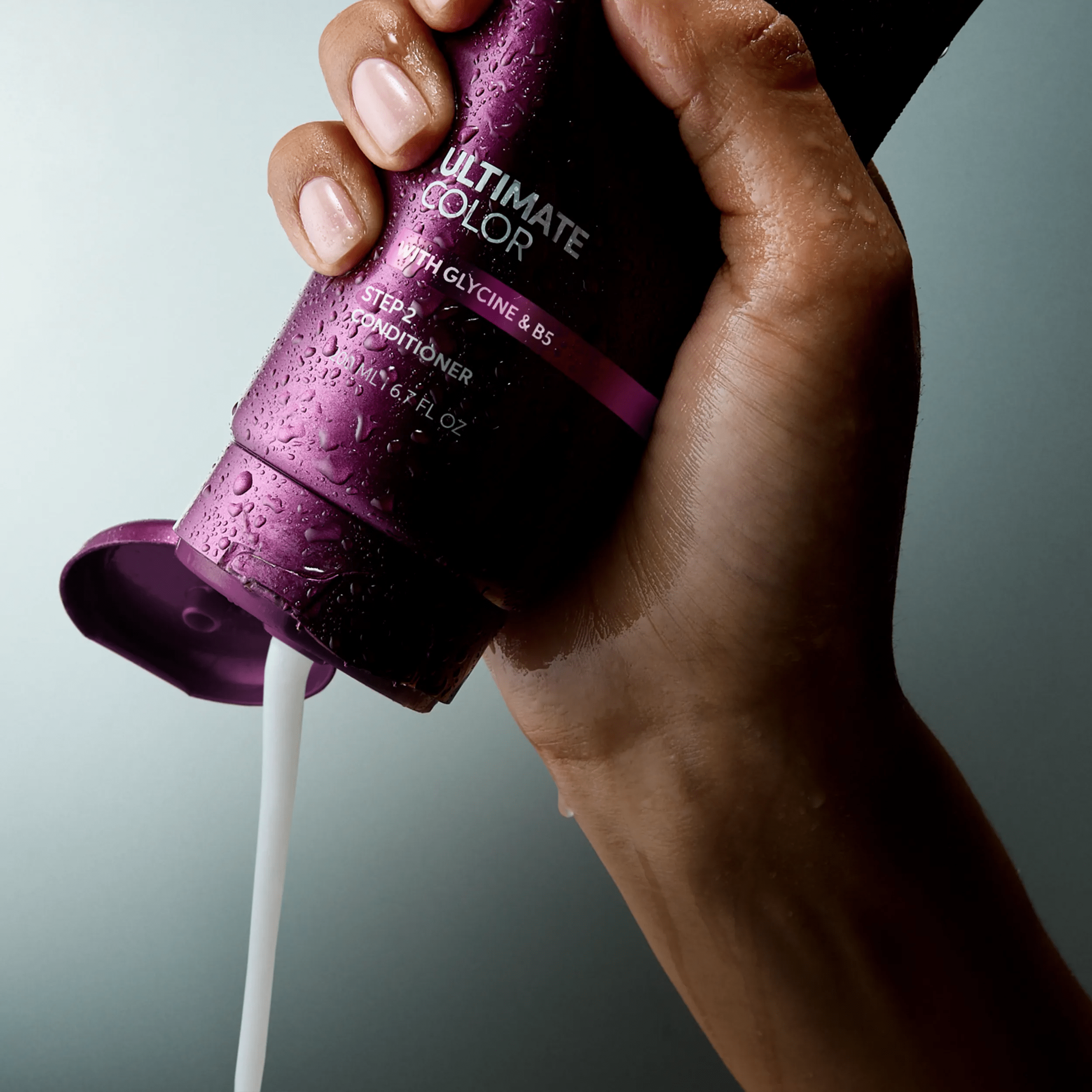 Image of model's hand squeezing a bottle of the Ultimate Color conditoner. Text overlay reads " Smooth, creamy texture for porous strands".