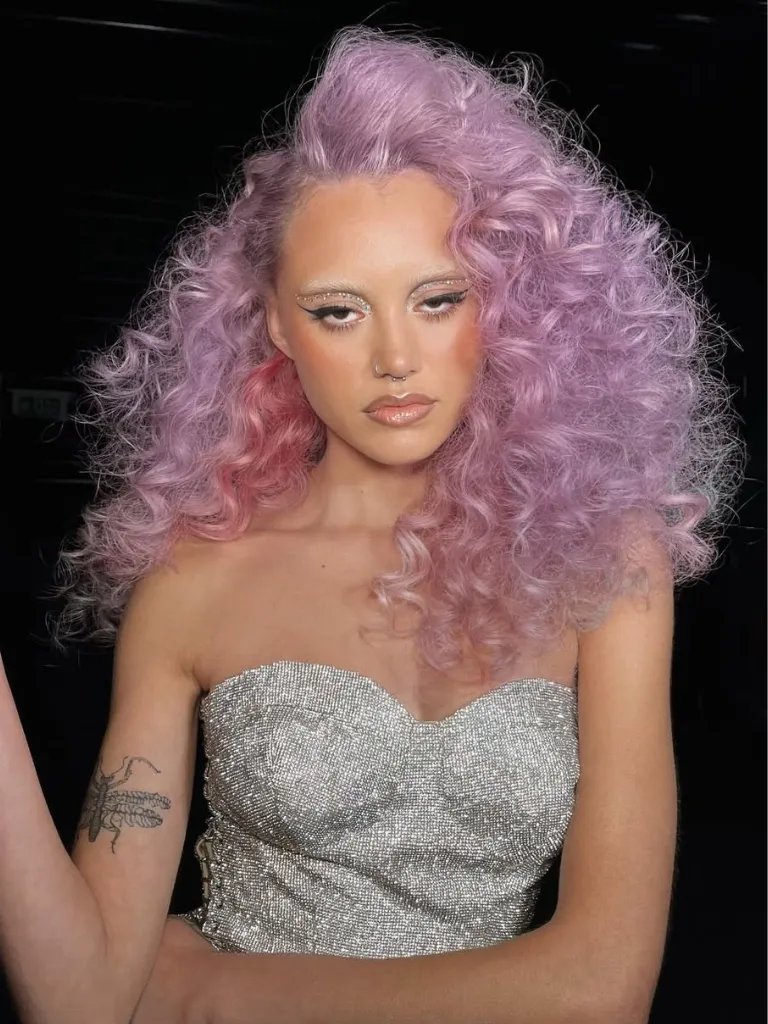 Model with full, voluminous, curly hair in shades of lilac and blush pink.