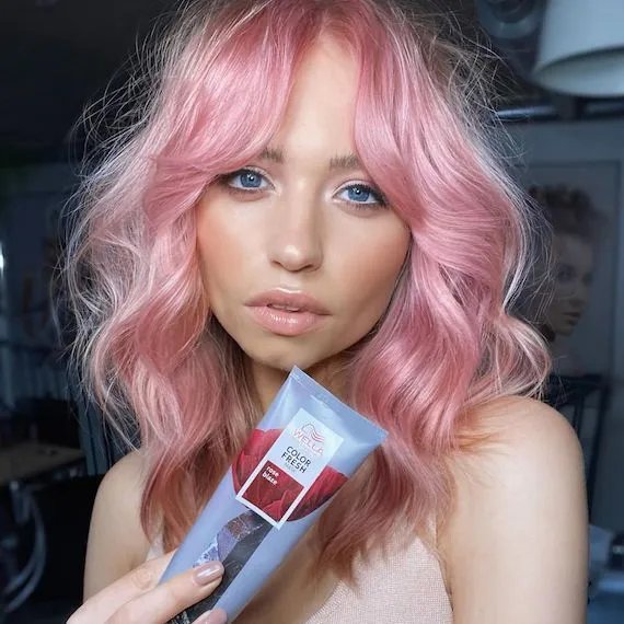 Model with wavy, candy pink hair holds up Color Fresh Mask in Rose Blaze.