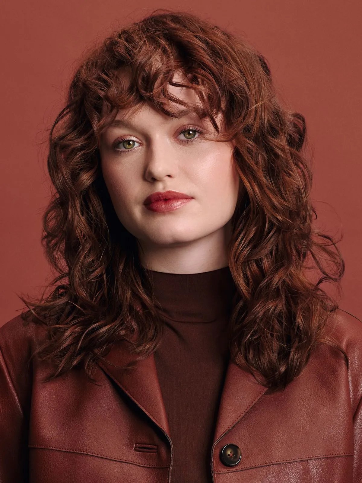 Model with rich copper red curls, wearing a red leather jacket against a red backdrop.