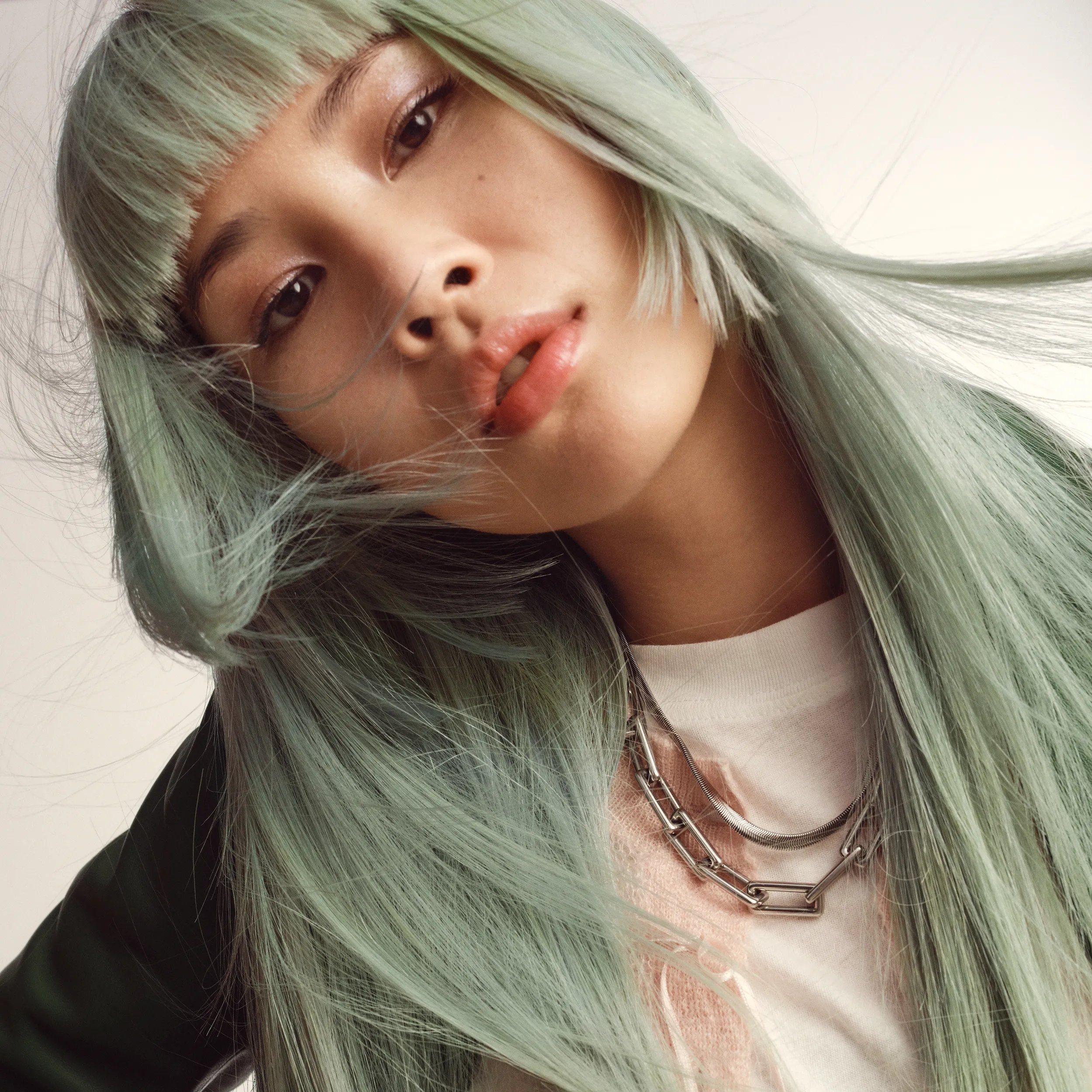 Woman with long mint green hair, blunt bangs, and a silver chain necklace.