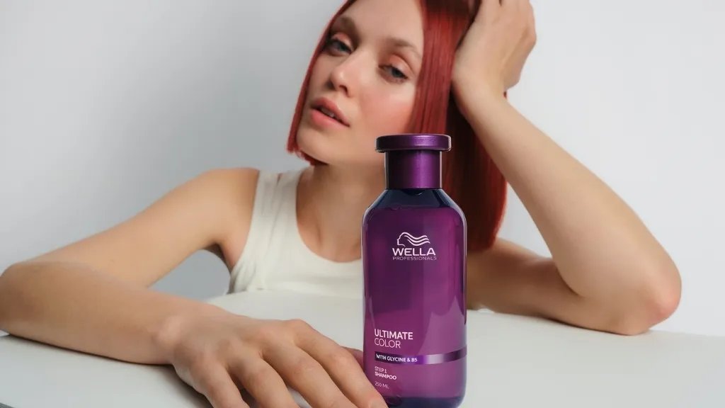 Red-haired model rests hand on a bottle of ULTIMATE COLOR Shampoo.