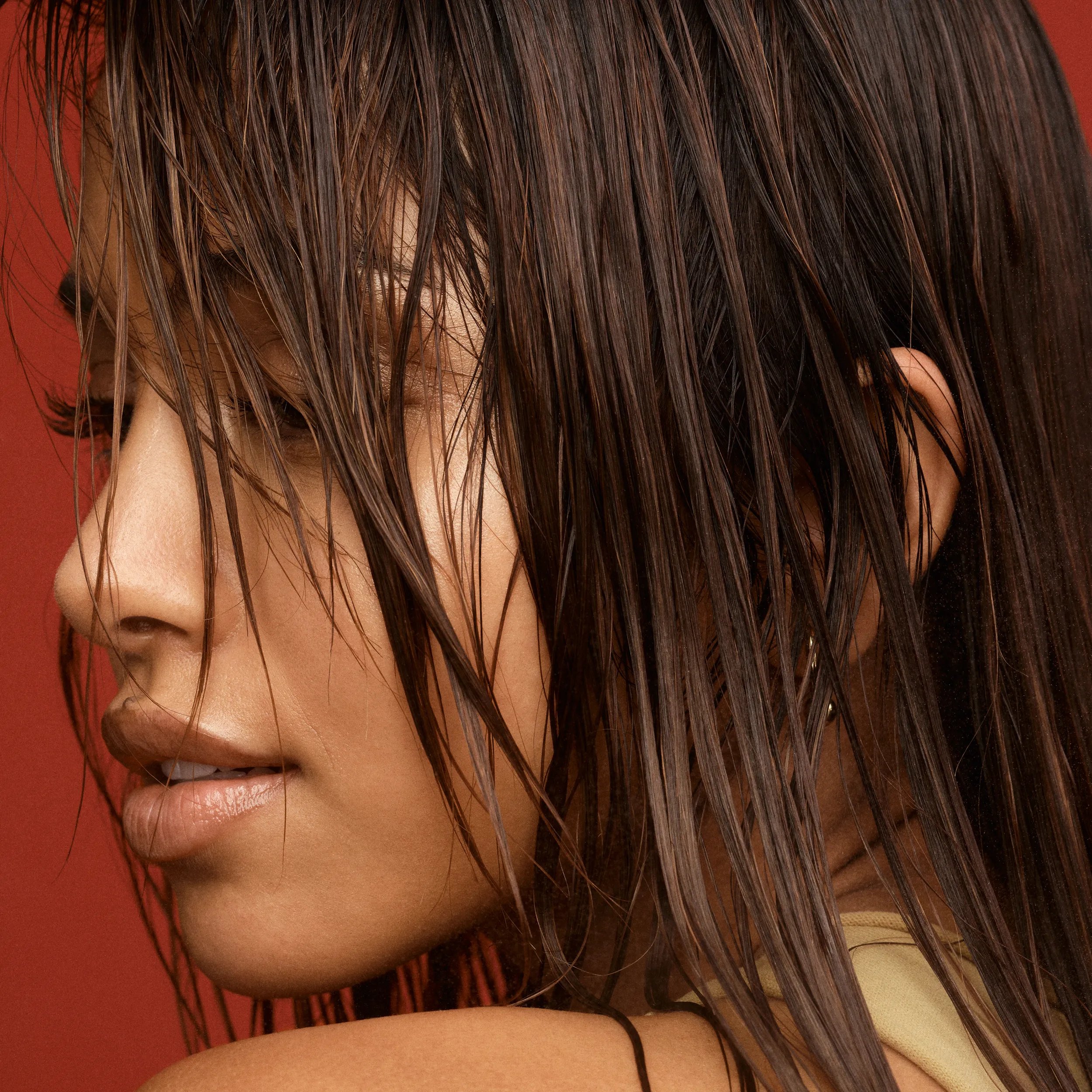 Close up of a woman with sleek, wet-look hair, showcasing a profile view against a vibrant red backdrop.