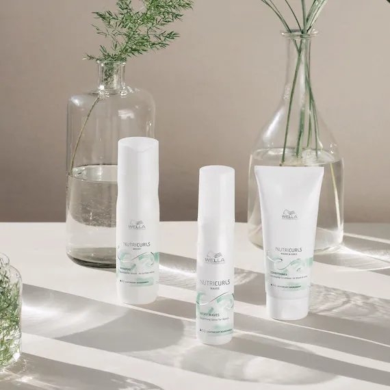 Collection of Wella NutriCurls products is on a white surface with glasses
vases behind them.