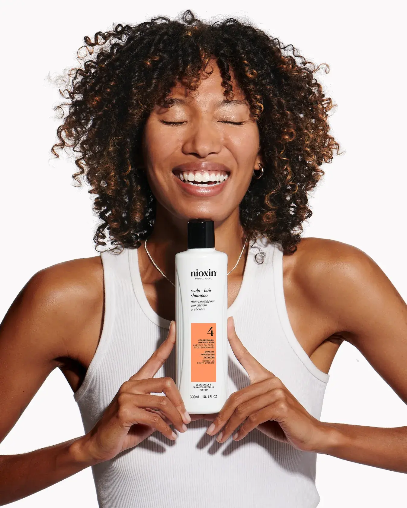 black woman with curly hair smiling holding Nioxin system 4 scalp + hair Shampoo with both hands