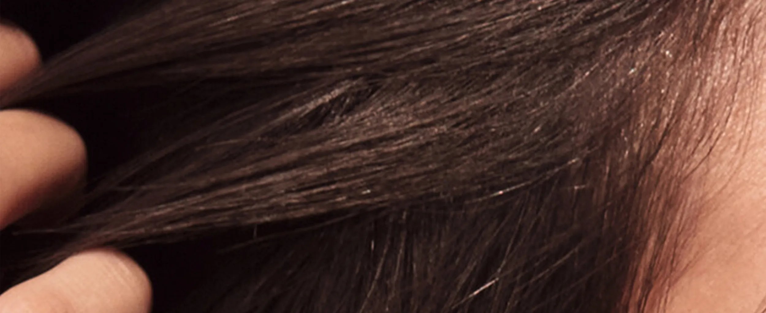 Close-up shot of dark brown, straight hair being lightly touched by a hand.