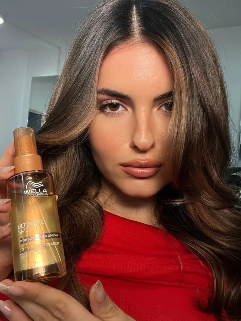 Model with dark brown, straight hair holding a bottle of ULTIMATE SMOOTH Miracle Oil Serum.
