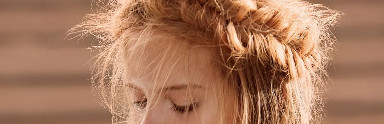 A close-up portrait of a young woman with light blonde hair styled in a loose, braided updo.