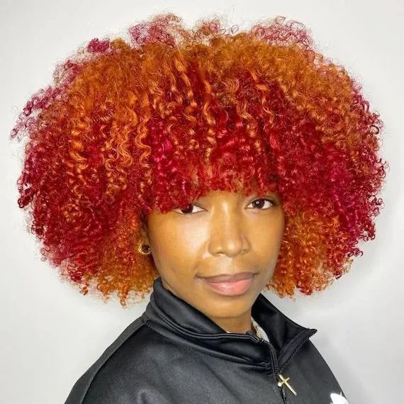 Model with mid-length, curly red and and orange hair smiles at the camera. 