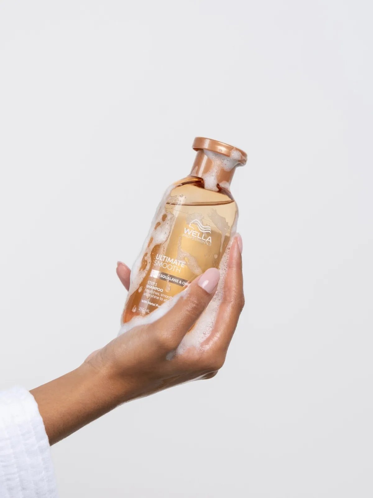 Model holds a bottle of ULTIMATE SMOOTH Shampoo.