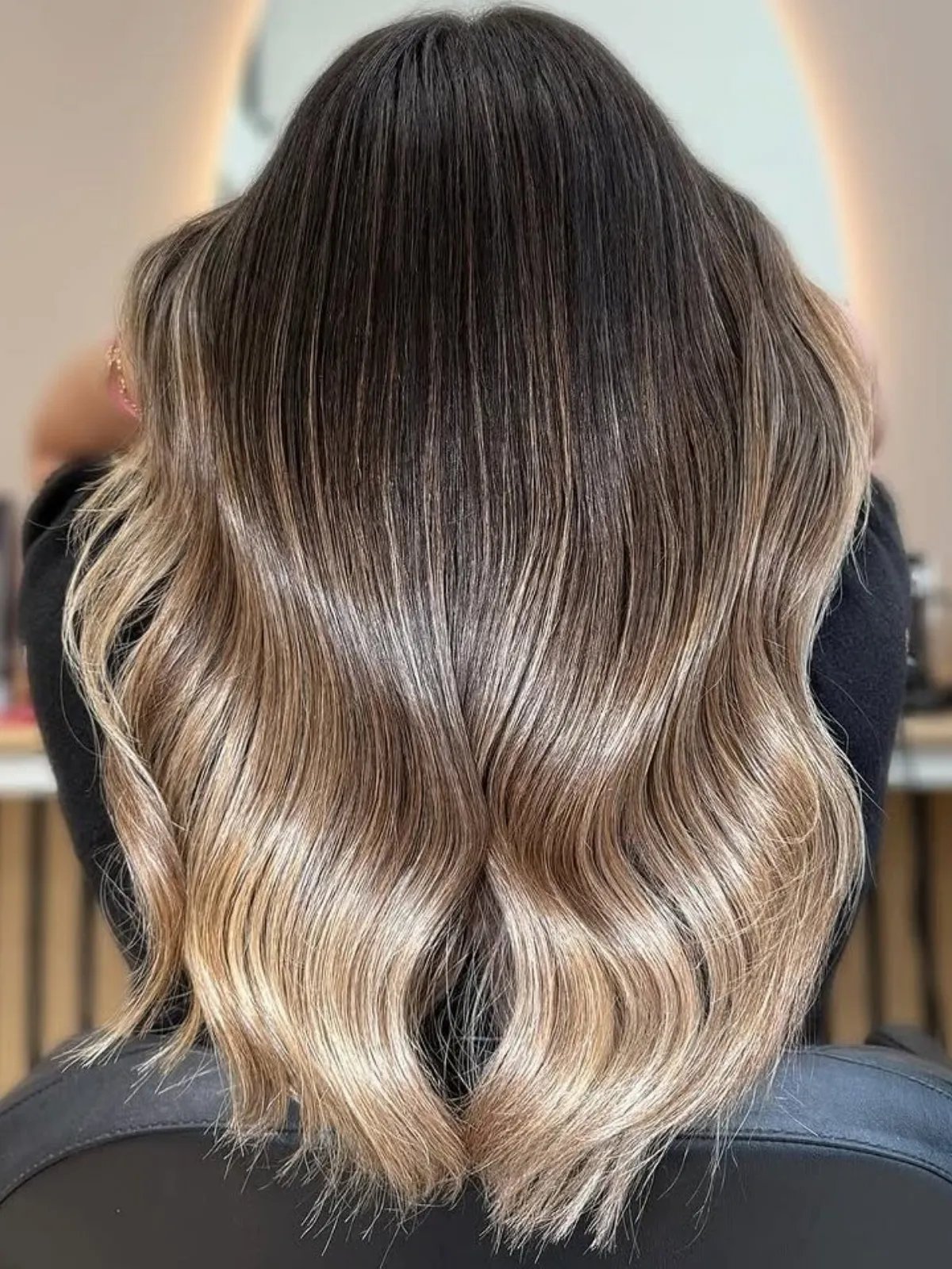 Model with neutral blonde ombre hair that graduates from dark brown at the roots to light on the ends.