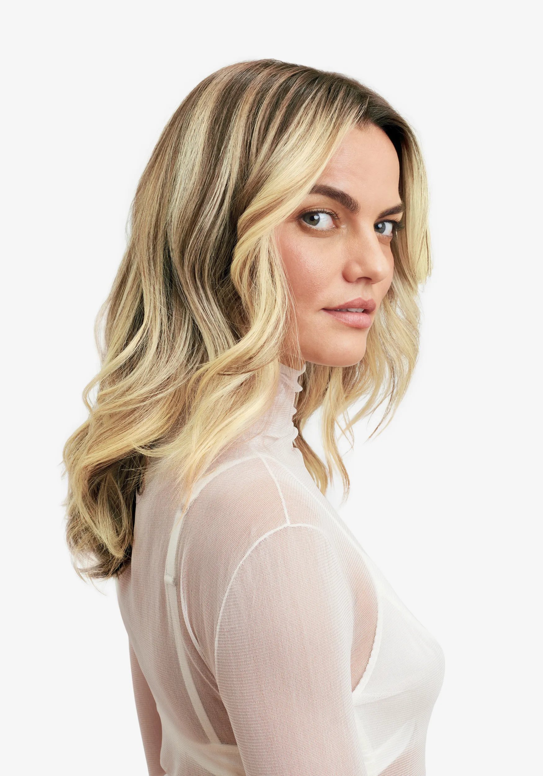 Side profile of model with shoulder length blonde, wavy hair, wearing a white turtle neck shirt.