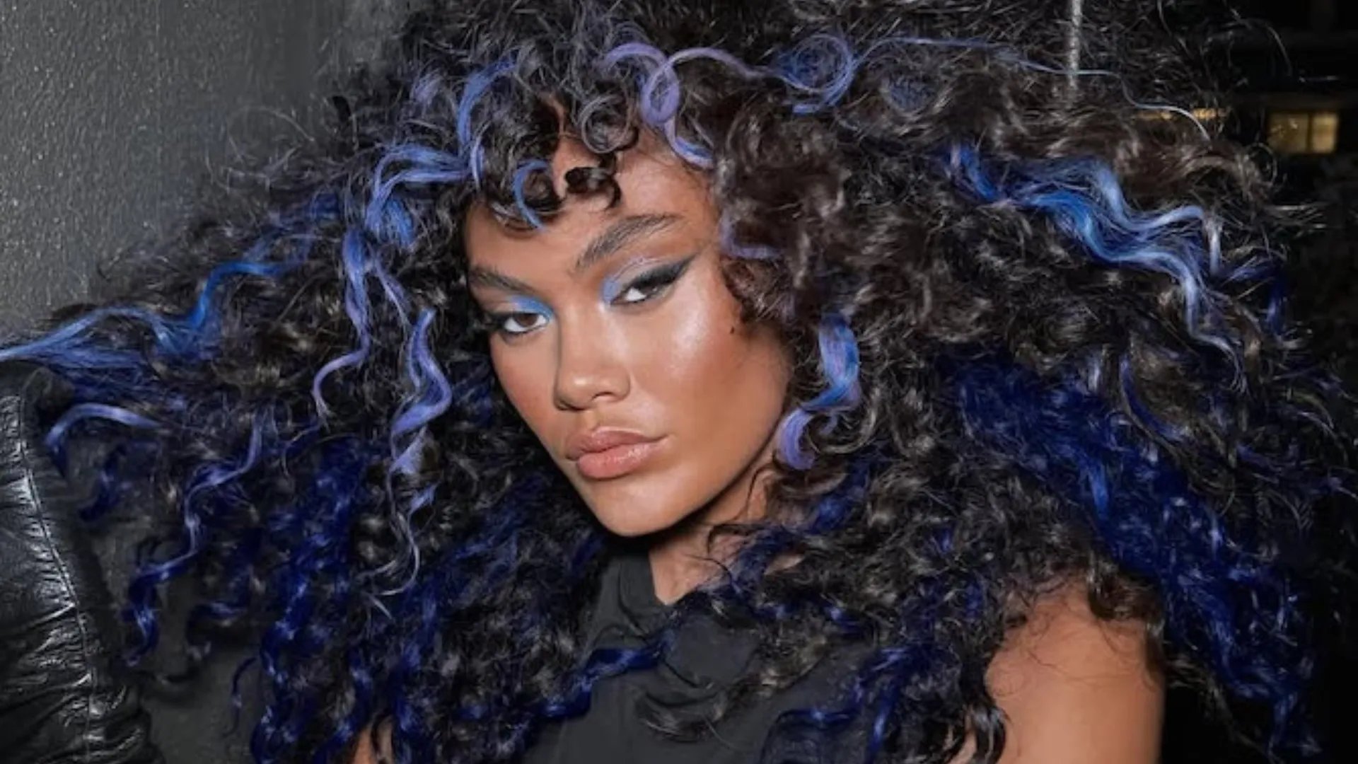 Model with black, curly hair featuring blue highlights.