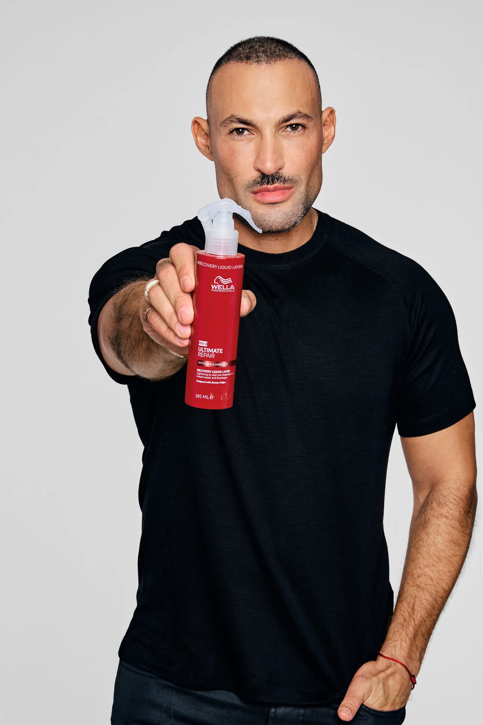 Image of Wella Professionals Global Ambassador Romeu Felipe. He is  dressed in black and holding up a bottle of Ultimate Repair Recovery Liquid Layer. 