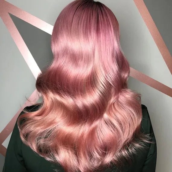 A person with glossy pink, wavy hair facing a grey and pink coloured wall