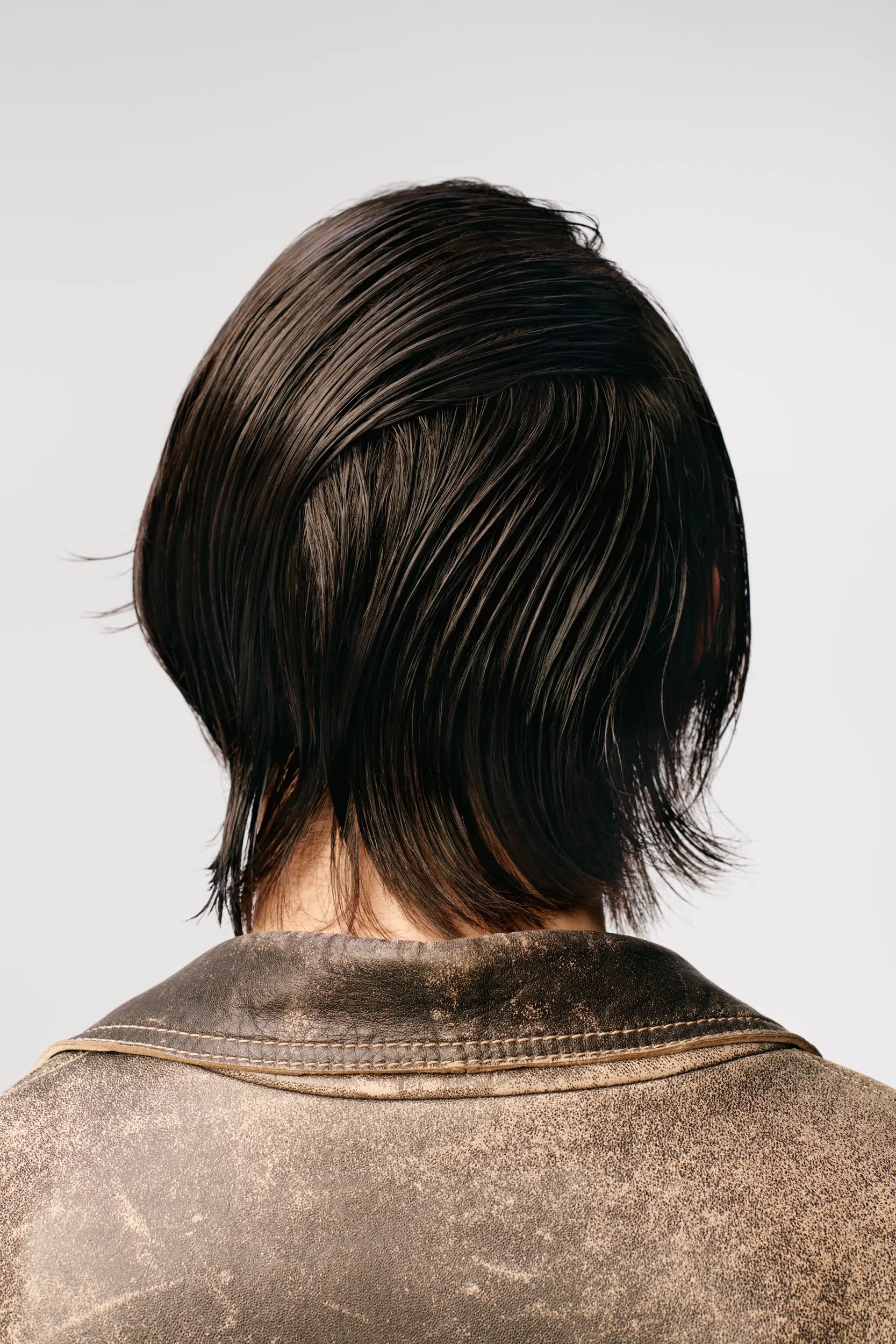 Image of a the back of a model's head on a white background. Model has short brunette hair in a wet-look style