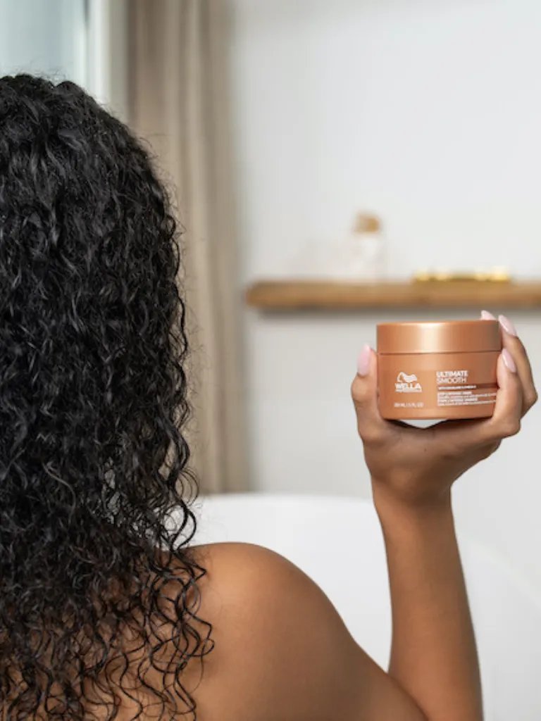 Model with dark brown, curly hair holding up ULTIMATE SMOOTH Mask.