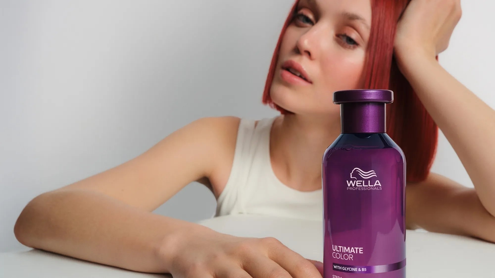 Model with bright red hair holds a bottle of ULTIMATE COLOR Shampoo.