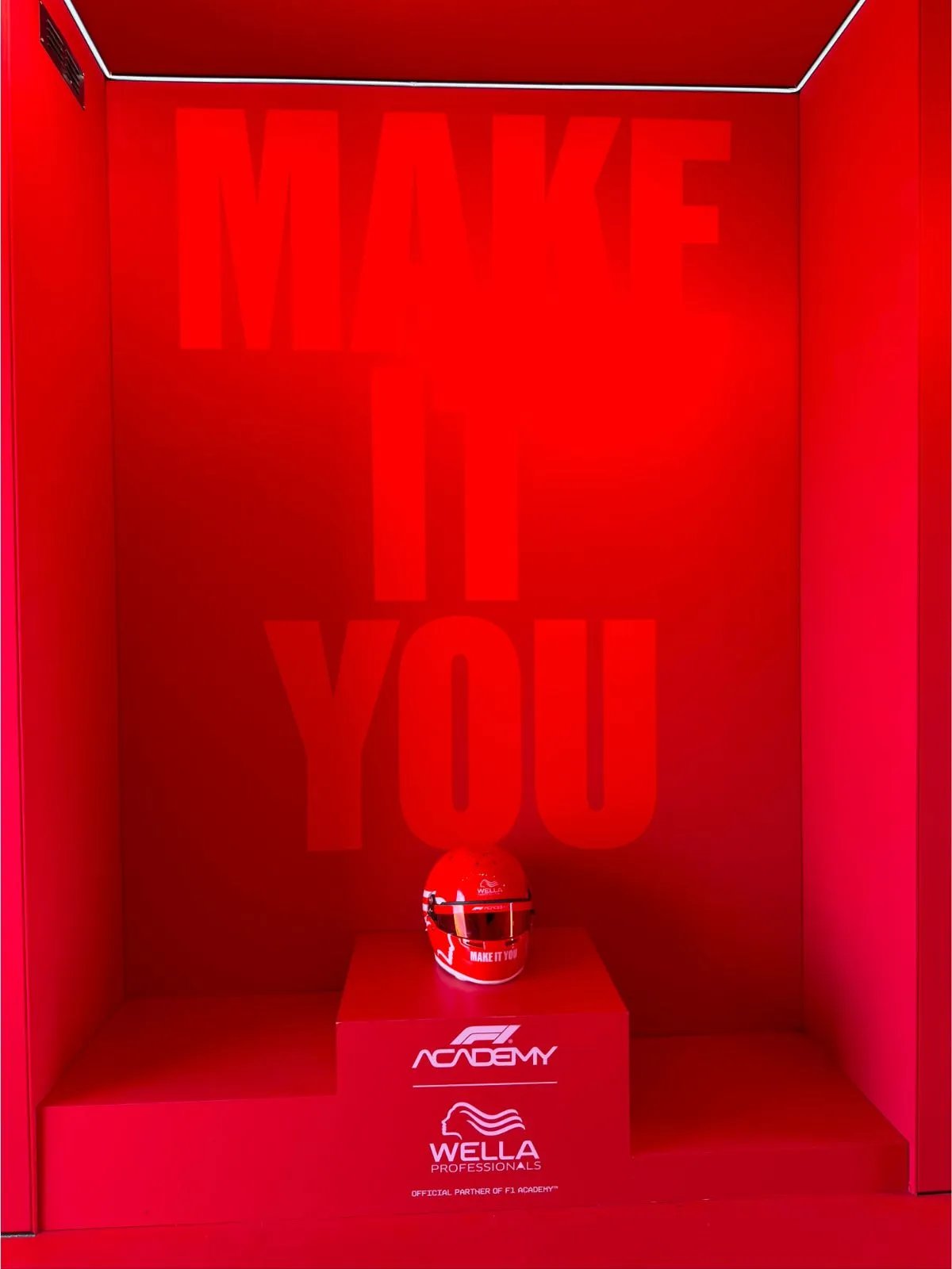 Red wall emblazoned with MAKE IT YOU and a Wella red racing helmet.