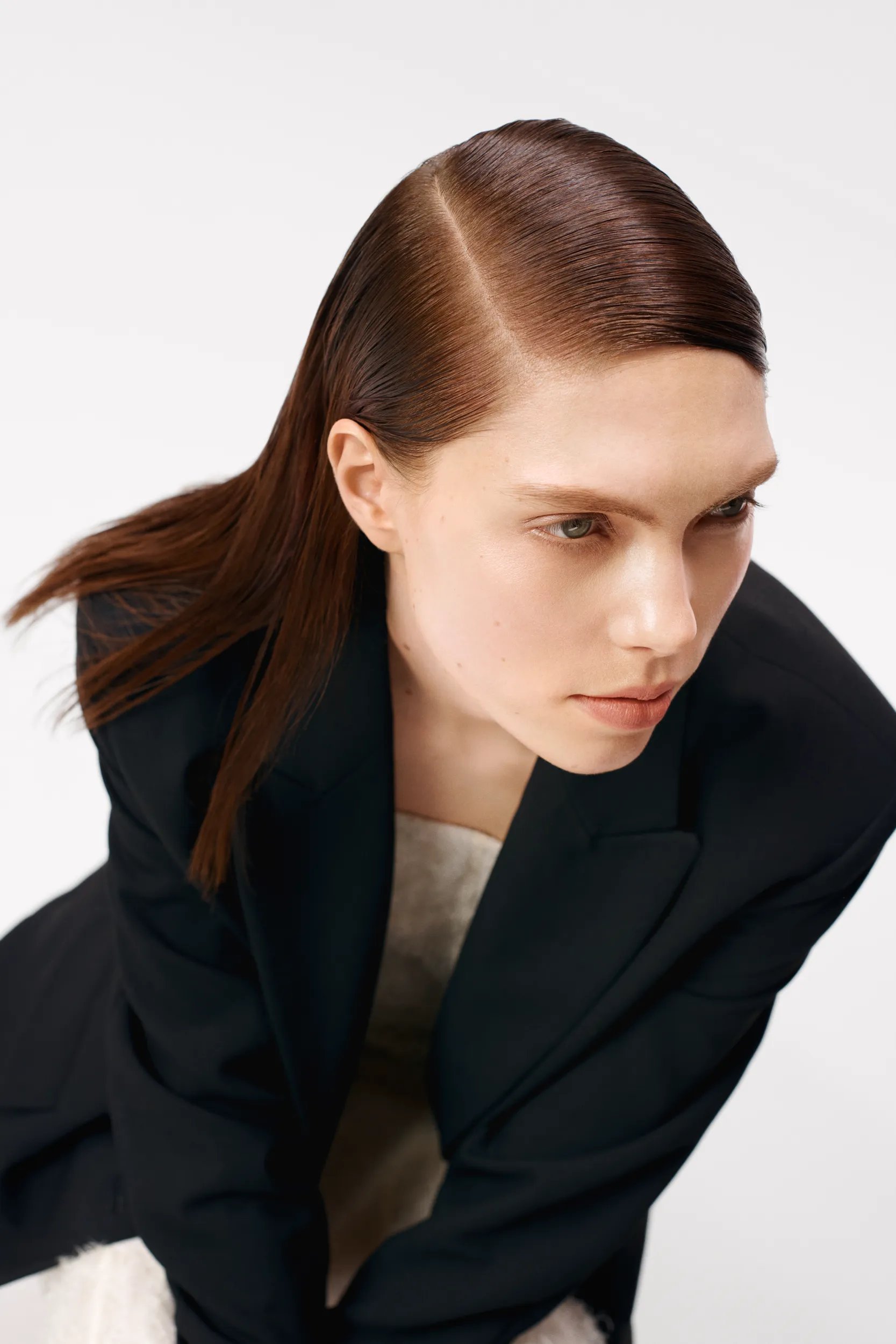 Aerial view of model with slicked red hair, wearing a black blazer, against a white background