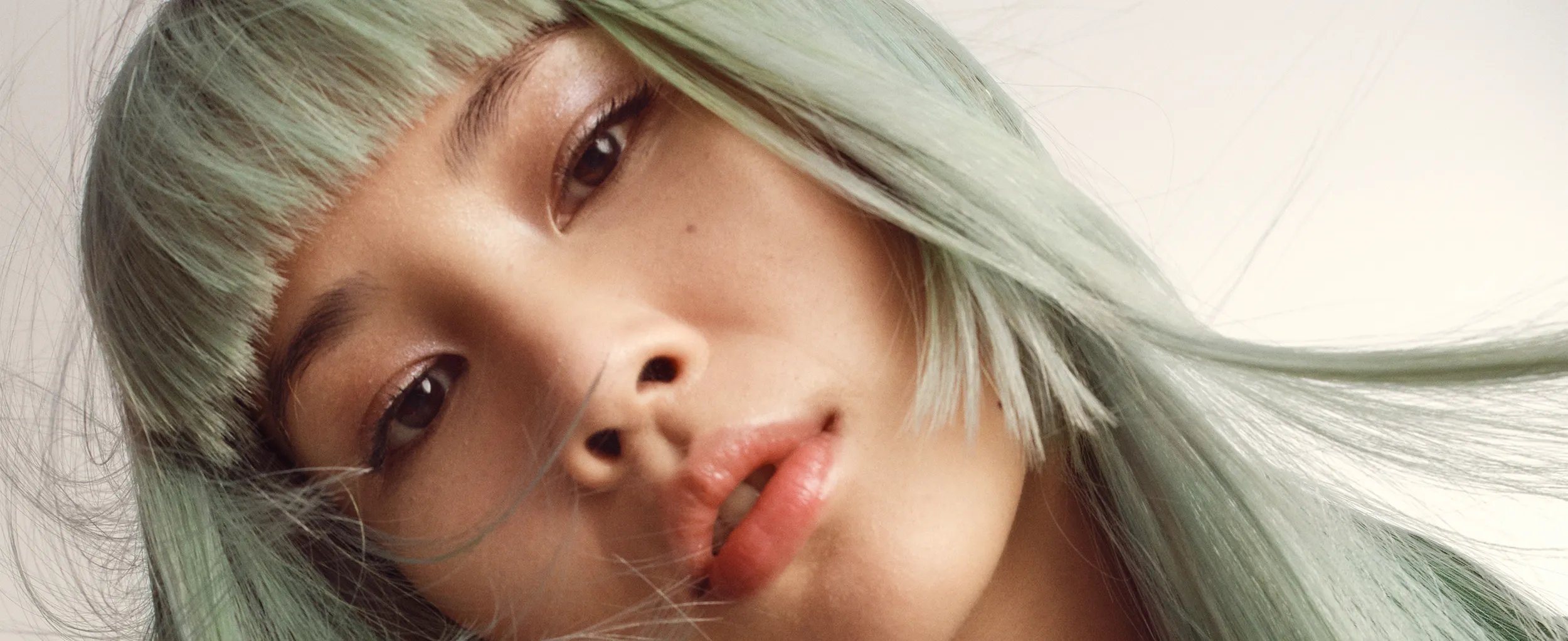 Woman with long mint green hair, blunt bangs, and a silver chain necklace.
