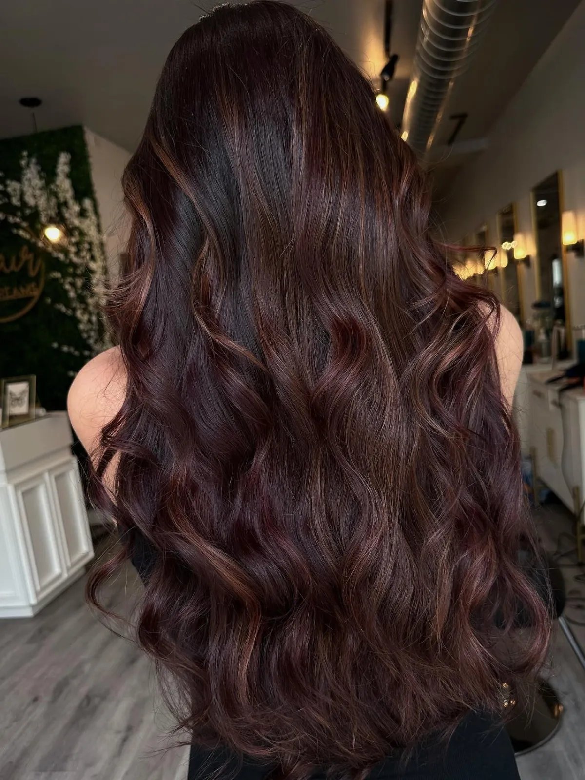 Model with long, dark, glossy brunette hair featuring maroon balayage.