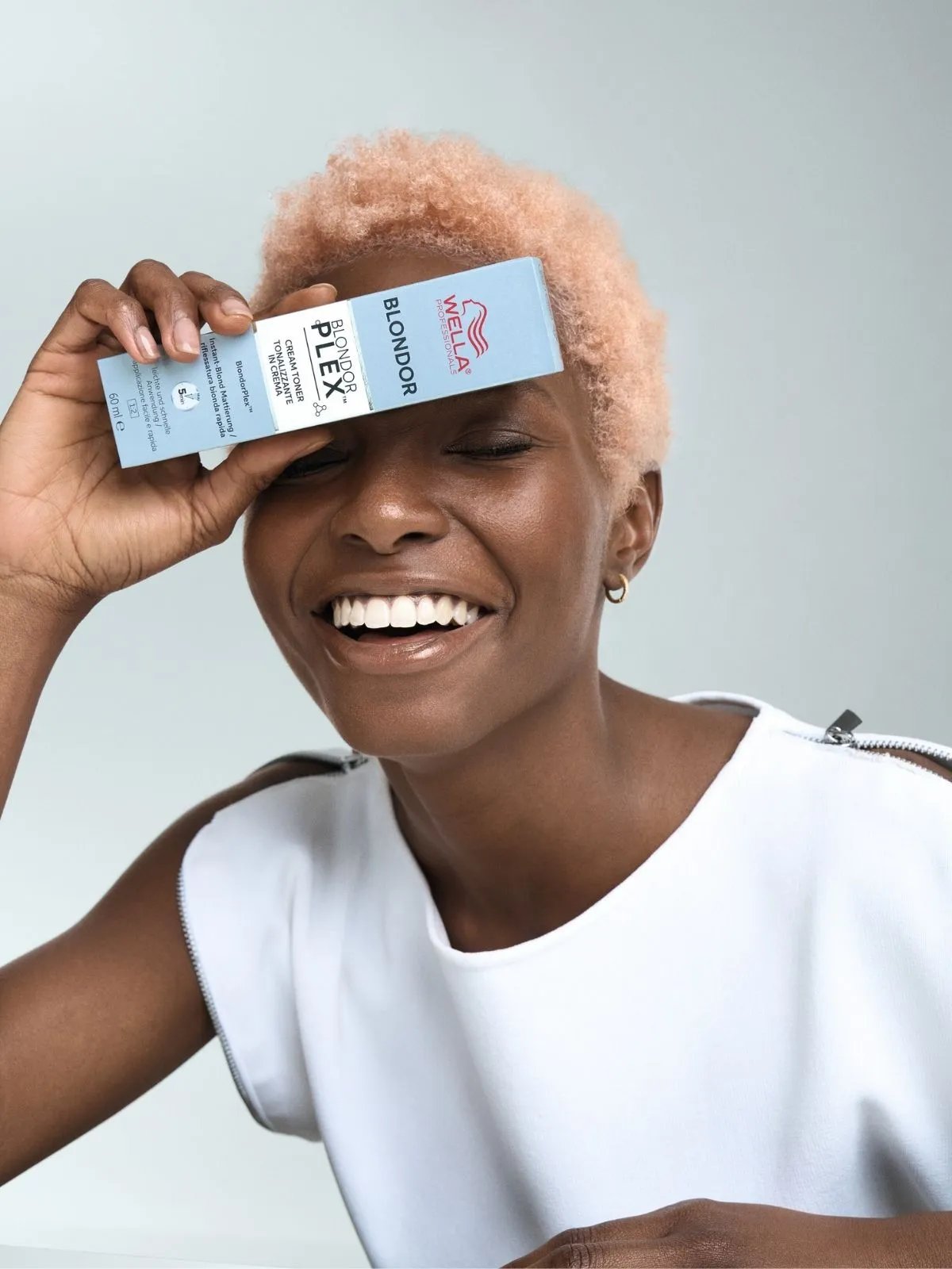 Model with rose blonde, coily hair holds up a box of BlondorPlex lightener.