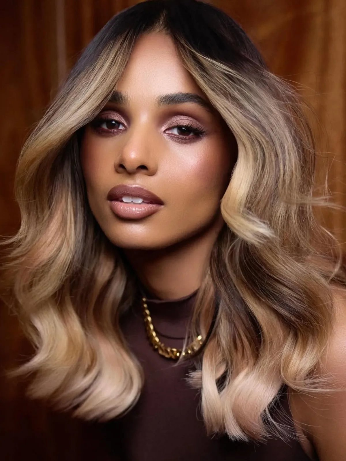 Model with loosely waved, glossy hair featuring dark roots and beige blonde lengths.
