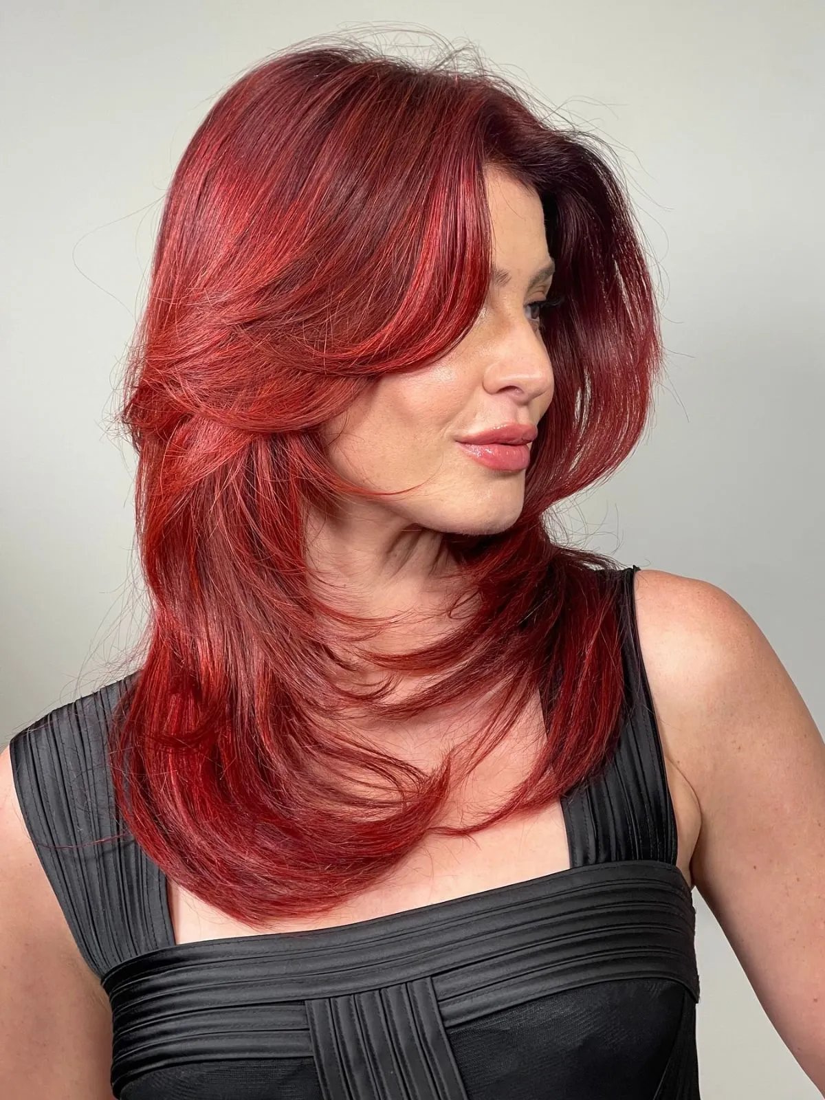 Model with bright cherry red hair styled in straight, feathered layers.