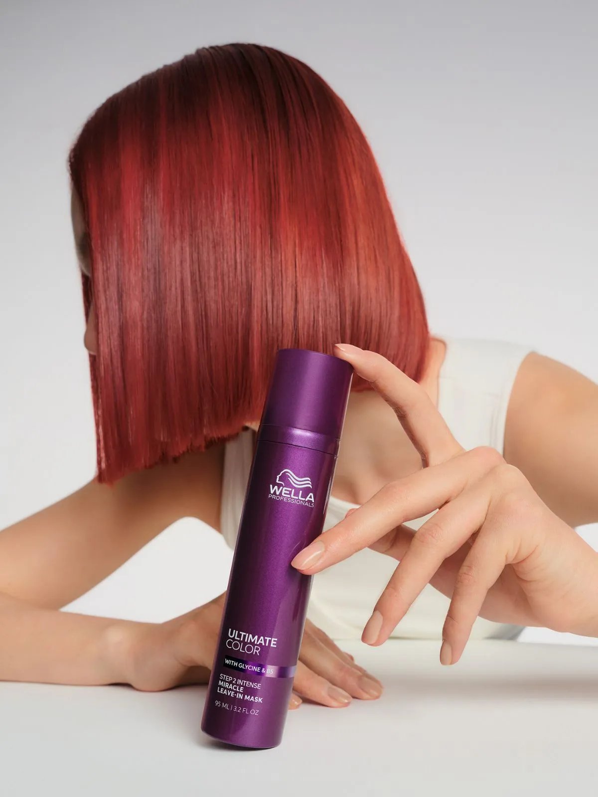 Model with red hair holds a bottle of ULTIMATE COLOR Miracle Leave-In Mask.