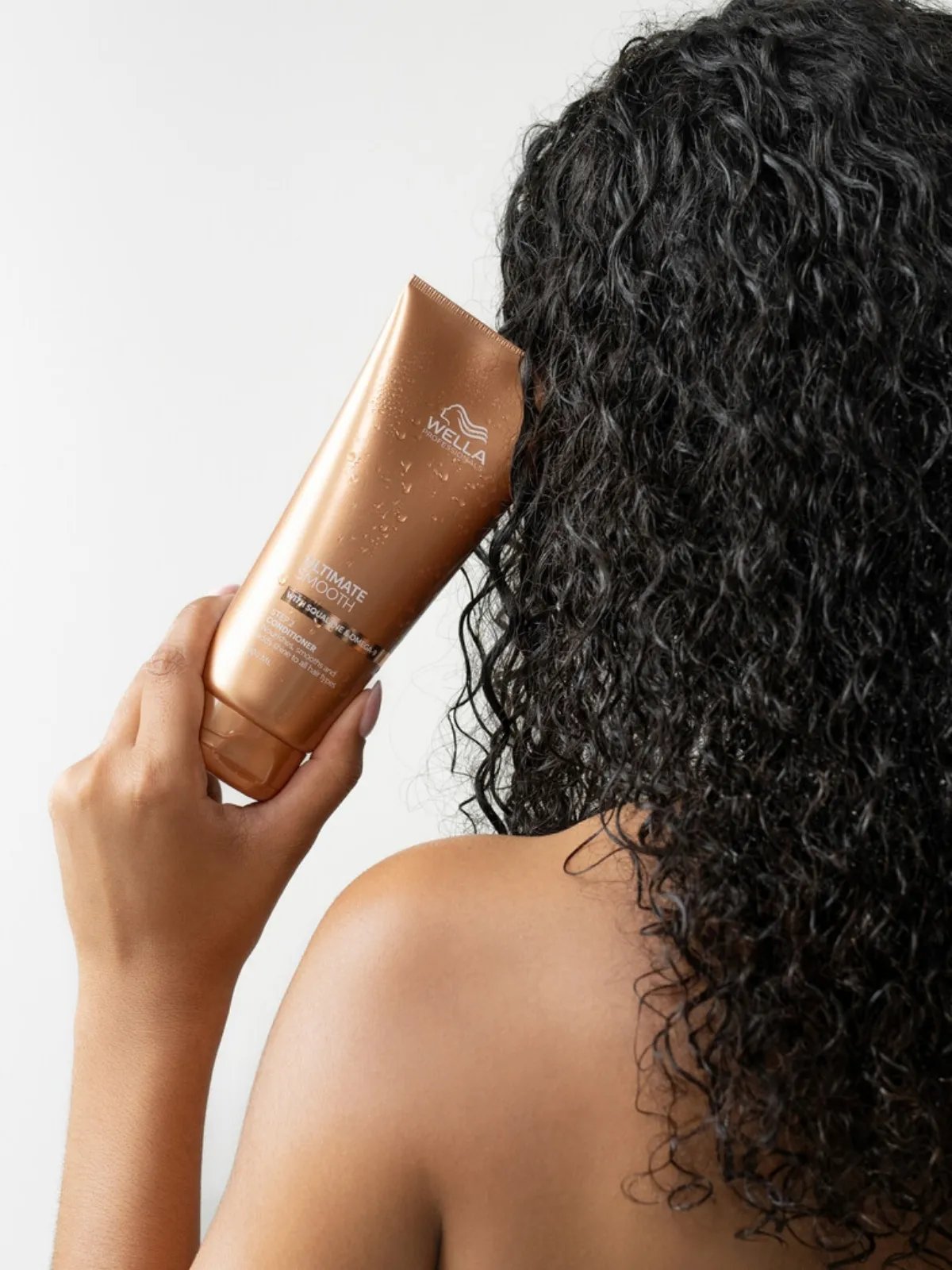 Model with dark, curly, damp hair holds up ULTIMATE SMOOTH Conditioner.