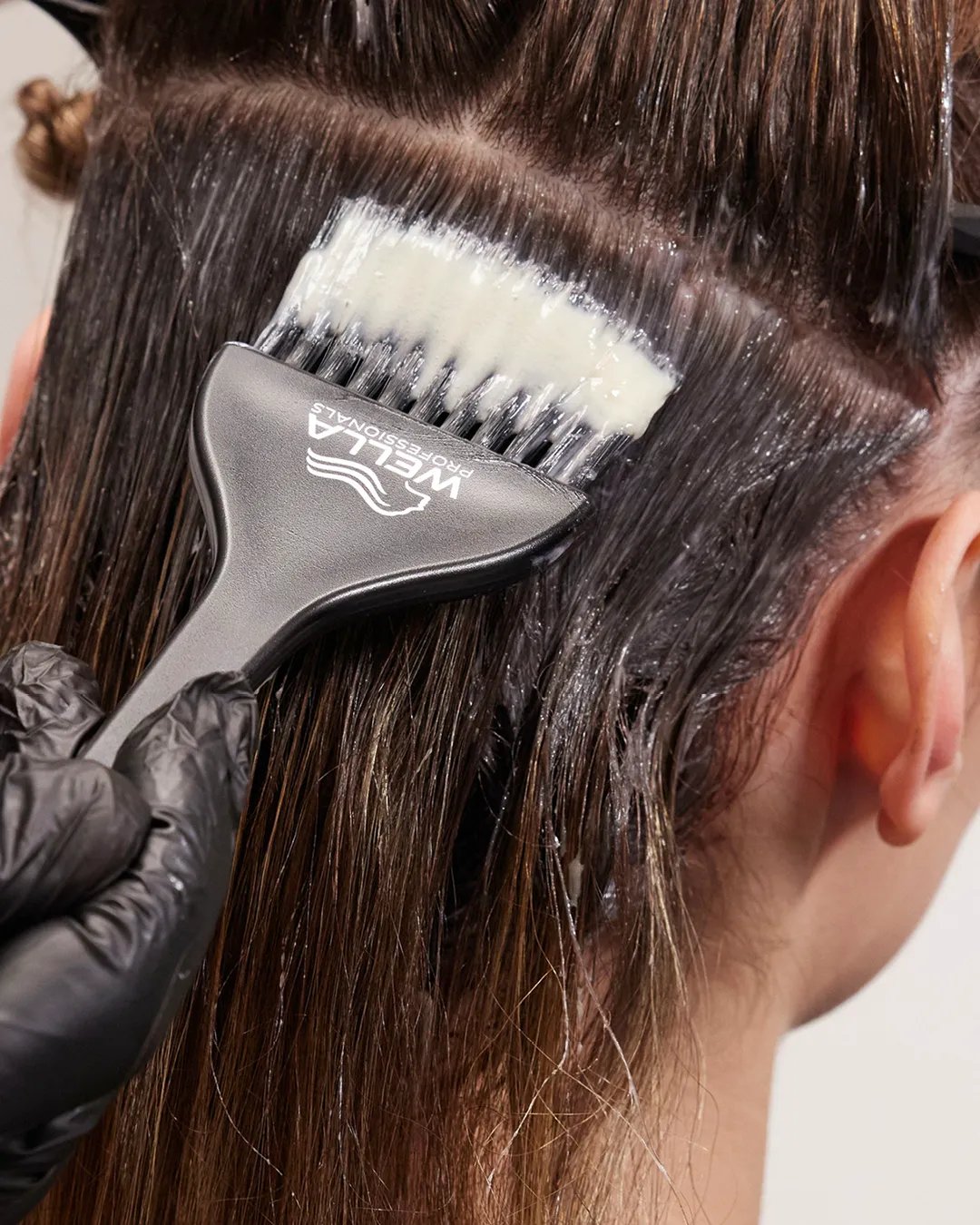 stylist wears gloves whilst applying hair lightener to their client’s hair in sections