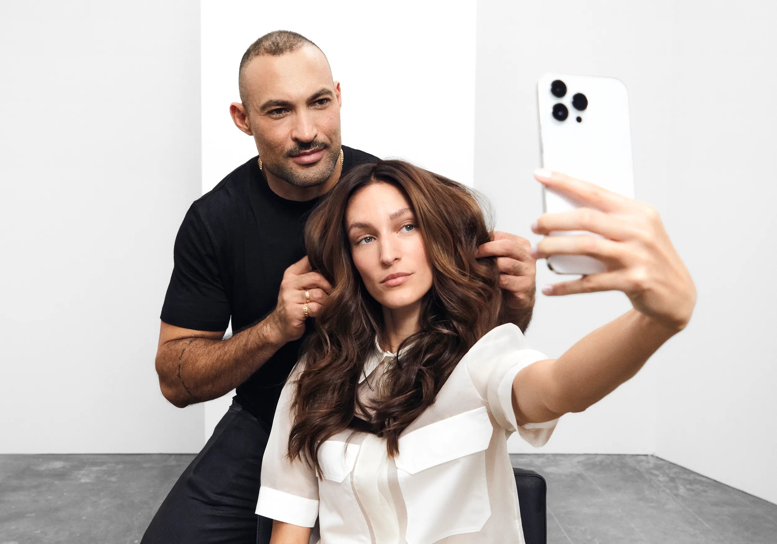 A womand and hairdresser pose for a selfie together in front of a mirror, enjoying the moment.